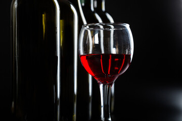 several different bottles of wine and a glass with red wine on a dark glossy background.