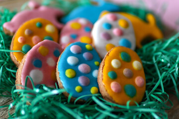 Close up of Easter cookies in the shape of a rabbit and colorful eggs on a log in the grass. Easter holiday concept food decoration