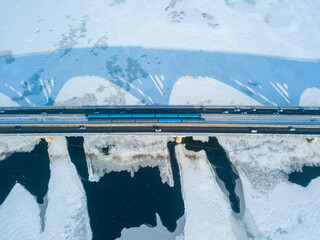 Two metro trains travel on Kiev metro bridge. A shadow falls on the frozen Dnieper River. Aerial drone view. Winter sunny morning.