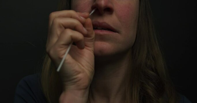 A young woman is taking a sample from her nose with a swab to test for corona virus