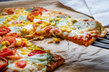Colorful fresh pizza hot from the oven with mozzarella cheese, corn, pesto and cherry tomatoes. Baked, delicious, gluten free pizza slice lifted with melted cheese. Ready to be served.