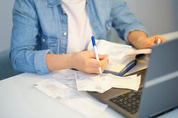 woman using a pen writing on bank account book while holding the bills to calculate in living room...