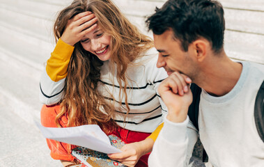 Outdoor shot of two young students studying together sitting on the stairs at the university. Two colleagues smiling, a young woman and a man learnig to the college campus together.