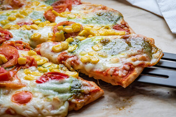 Close up on colorful fresh pizza hot from the oven with mozzarella cheese, corn, pesto and cherry tomatoes. Baked, delicious, gluten free pizza sliced and placed on a baking sheet. Ready to be served.