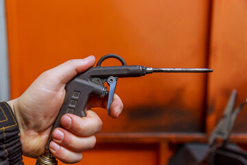 A blow gun in the hand of a worker, A gun for an air compressor in a factory.