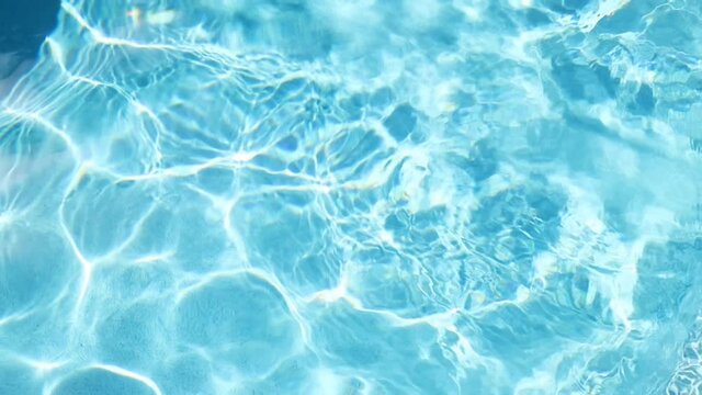 beautiful dramatic scenic bright vibrant blue clear water of pool ripples with warm sun shining light reflection on water surface on bright warm summer day. Holiday travel spa resort concept