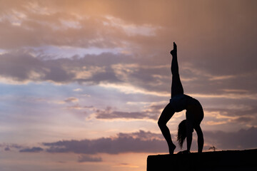 Flexible girl doing exercise on sky background during dramatic sunset