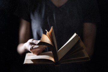 Hands hold Vintage open Book Glows on black background. Concept of reading, knowledge and open mind