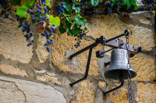 Campana y parra con uvas en una casa de piedra de una aldea hist&oacute;rica medieval francesa