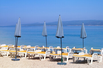 Blue umbrellas and chaises for relax on sea coast. Summer vacations and travel concept. Paid service on beaches.