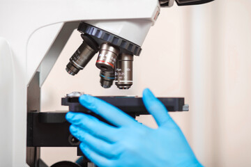 laboratory assistant in blue gloves examines a semen sample under a microscope. Shallow depth of...