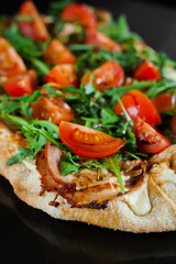 Pinsa romana gourmet italian cuisine on black background. Scrocchiarella traditional dish. Food delivery from pizzeria. Pinsa with meat, arugula, tomatoes, cheese.
