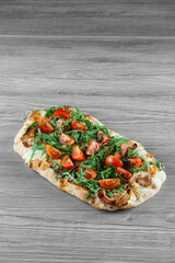 Scrocchiarella gourmet italian cuisine on grey wooden background. Pinsa romana traditional dish. Food delivery from pizzeria. Pinsa with meat, arugula, tomatoes, cheese.