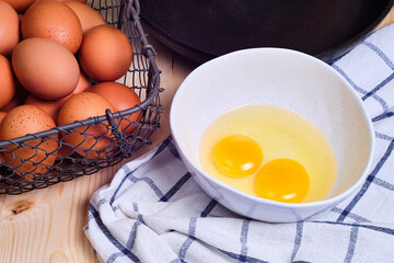 Eggs in a metal basket, in a white bowl, fryind pan and a tea towel on a wooden background.