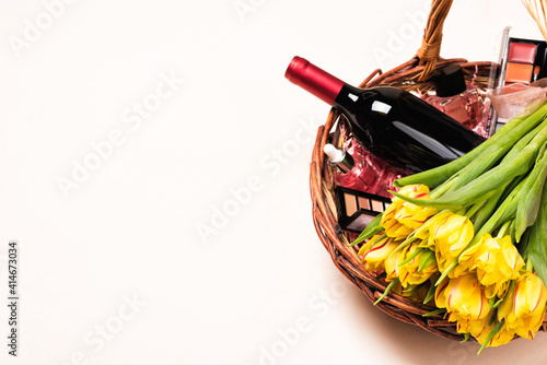 Bottle of red wine, tulip flowers and cosmetic in gift basket for Women's day and month, Mother's Day, birthday