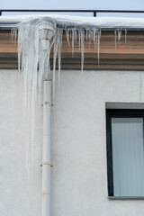 The roofs of the buildings are covered with snow and ice after a big snowfall. Huge icicles hang from the facades of buildings. The fall of icicles carries a danger to people's lives.