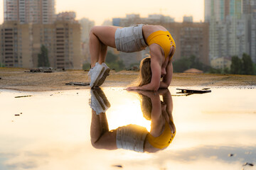 Flexible female gymnast doing handstand and calisthenic with reflection in the water on cityscape...