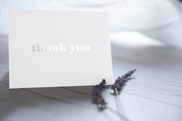 Thank you card  on wooden table with a pair of lavender flowers. Elegant minimalist composition with white background. Special thank you note.