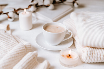 Fototapeta na wymiar Details of still life in the home interior of living room. Cup of coffee, cotton, book, candle, sweater. Moody. Cosy autumn winter concept on white background. Decoration.