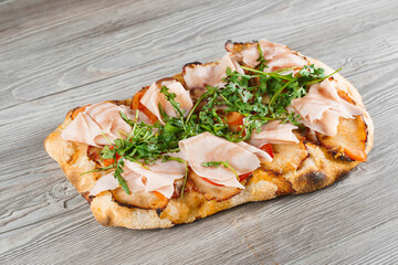 Scrocchiarella gourmet italian cuisine on grey wooden background. Pinsa romana traditional dish. Food delivery from pizzeria. Pinsa with meat, arugula, cheese.