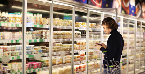 young man shopping in supermarket, reading product information.