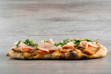 Scrocchiarella gourmet italian cuisine on grey wooden background. Pinsa romana traditional dish. Food delivery from pizzeria. Pinsa with meat, arugula, cheese.