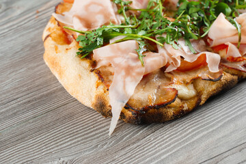 Scrocchiarella gourmet italian cuisine on grey wooden background. Pinsa romana traditional dish. Food delivery from pizzeria. Pinsa with meat, arugula, cheese.