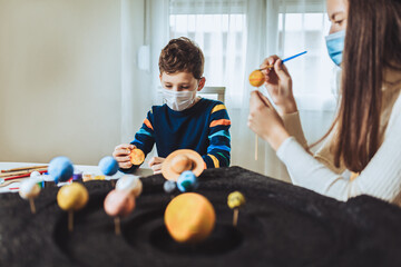Happy school boy and girl with protective mask making a solar system for a school science project at home