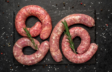 raw grilled sausages with spices on a knife on a stone background