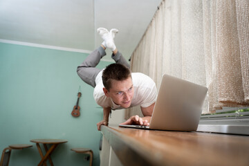 A muscular man practice yoga on one hand and works at a laptop. Self-isolation, remote working and healthy lifestyle concept