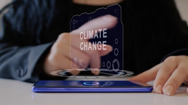 Female hand interacts HUD hologram with text Climate Change. Woman in black uses conceptual holographic technology of the future on the screen of a smartphone lying on a table