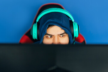 The gamer sits on a gaming chair and plays computer games. The player has turquoise headphones on his head © Anastassiya 