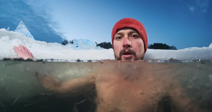 Winter swimmer portrait. Young man swims in the icy water turns his head and looks at the camera