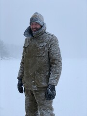 Naklejka premium smiling frozen man in the snow looking at the camera in the winter forest after a snow storm immunity and cold