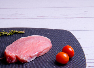 Pork steaks on a black chopping board and spices, cherry tomatoes, rosemary, peppercorns, copy space