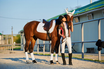 Beautiful horse rider girl stands near a horse on a farm   