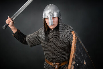 A medieval warrior in chain mail and a helmet with a sword and shields in his hands posing against...