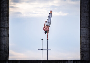 Circus artist keeps balance on one hand on the sky and industrial construction background. Concept...