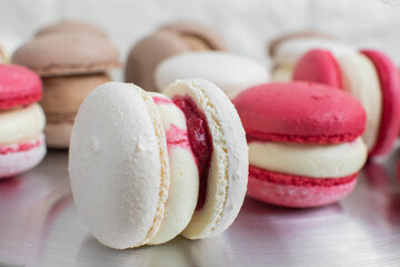 Colorful fresh tasty delicious macarons on the table, close up shot. Focus on white big macaroon with white cream and red berry jam
