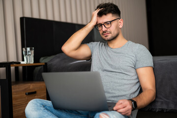 Handsome bearded confused man dressed elegant sitting on the floor at home and holding hand on head...