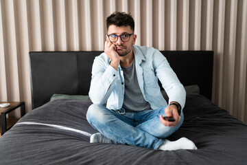 Nothing interesting to watch. Handsome young man holding remote control and looking bored while watching TV on the couch at home