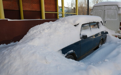 blue old car under a snowdrift in a parking lot