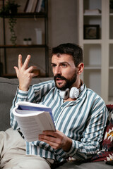 Fototapeta premium Young man reading a book on the couch. Man relaxing in the living room.