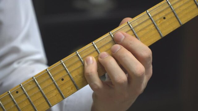 Guitarist's fingers on the neck of a six-string electric guitar
