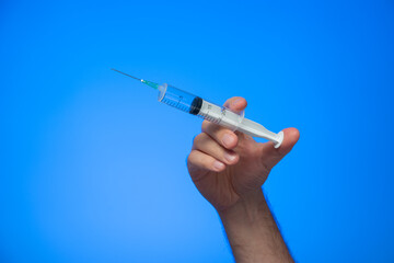 Disposable syringe with needle held in hand by Caucasian male hand studio shot isolated on blue background