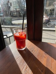 Glass of tomato juice in the afternoon sunlight on a wooden table, long shadow.