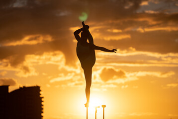 Silhouette of flexible and fit girl standing on fit with split and keeping balance against dramatic sunset Concept of yoga and healthy lifestyle 