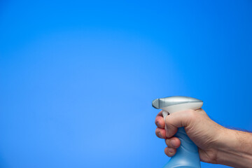 Caucasian male hand squeezing a plastic bottle spray nozzle isolated on blue background studio shot