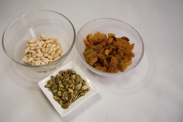 raisins, pumpkin seeds, peanuts in a transparent bowl on a white background
