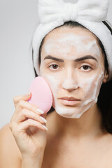naked woman using cleansing brush for face deep cleaning . Beautiful woman clean face with...